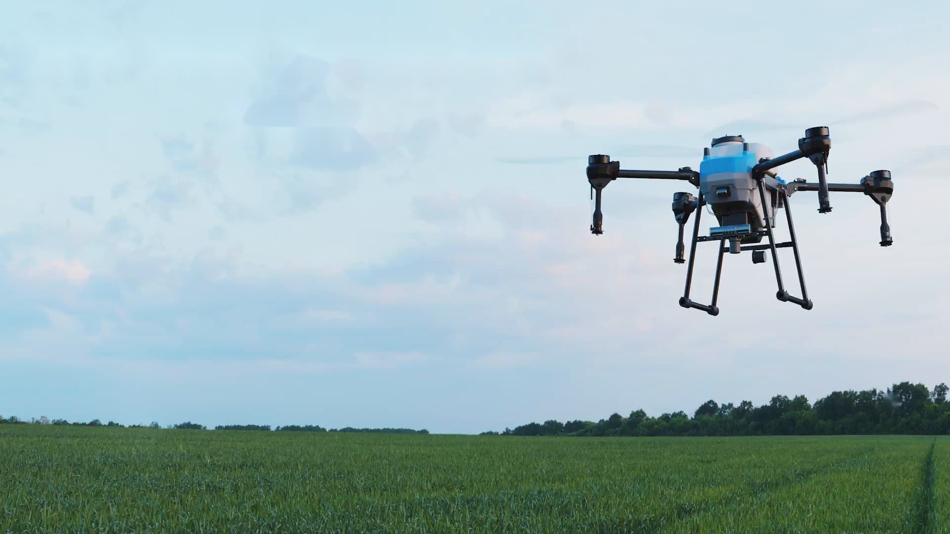 Industrial agriculture spray drone hovering over a green crop field at dusk.